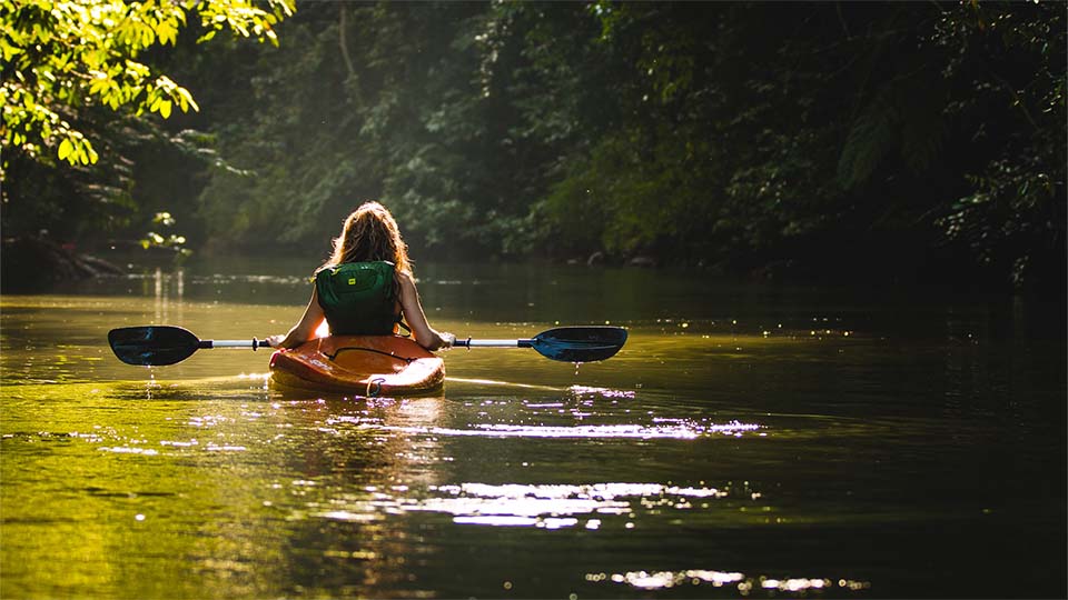 Auf dem Bild ist eine erfahrene Kanufahrerin auf dem malerischen Fluss Neckar zu sehen. Sie sitzt in einem robusten Kajak und paddelt mit geschmeidigen Bewegungen durch das ruhige Gewässer. Die Sonne spiegelt sich auf der glitzernden Oberfläche des Flusses wider, während sanfte Wellen das Boot leicht schaukeln.